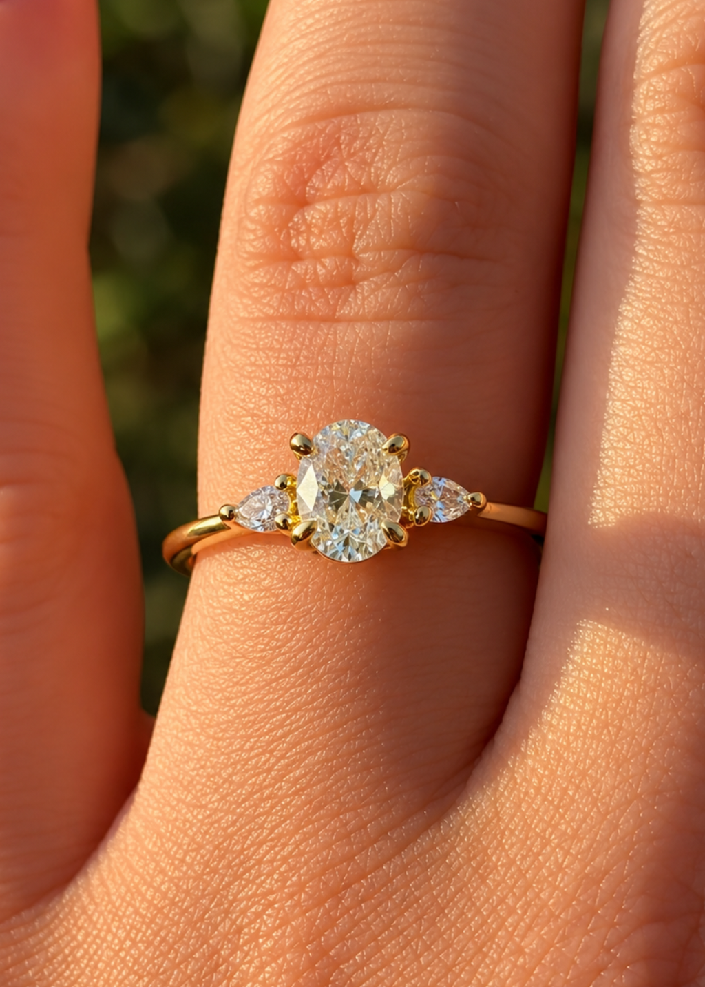 A yellow gold three-stone ring with a round center diamond and pear side diamonds, shown worn on a finger.